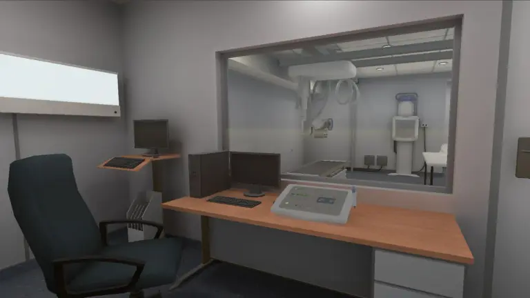 Vista desde la cabina de control virtual en el simulador de radiología, mostrando el escritorio con monitores, teclado y consola de mando frente al ventanal de plomo que da a la sala de rayos X.